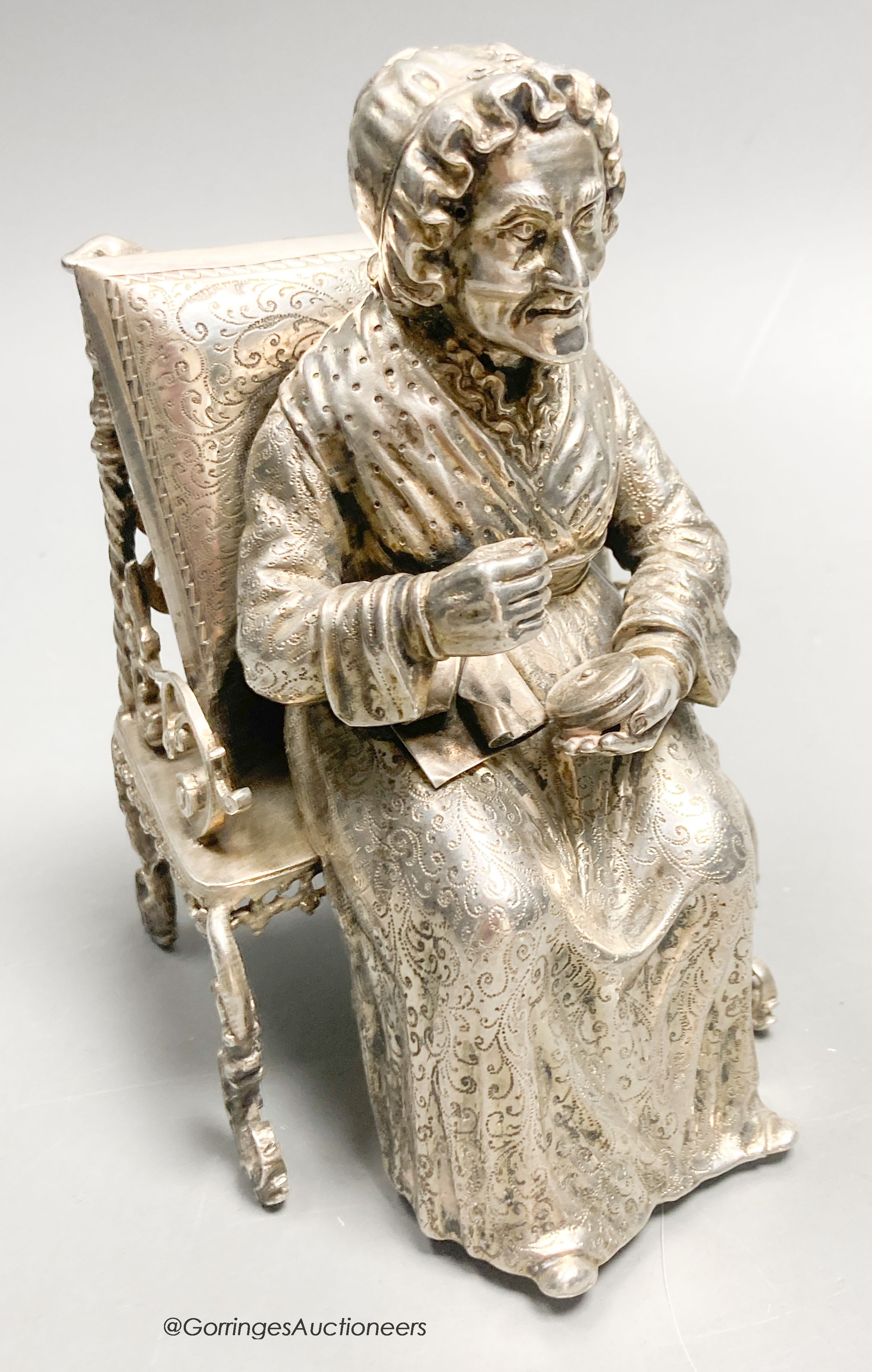 A late 19th century Hanau? white metal miniature model of an elderly lady seated in an armchair with cushion, engraved verso '1553, height 13.5cm